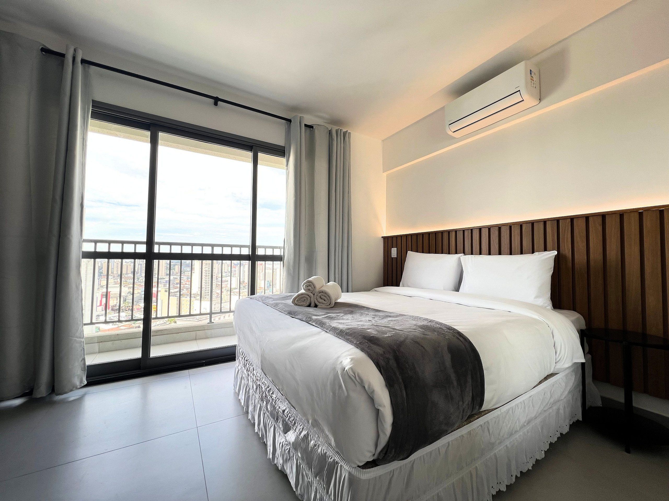 A hotel room with a large bed, a view of the city, and an air conditioning unit.