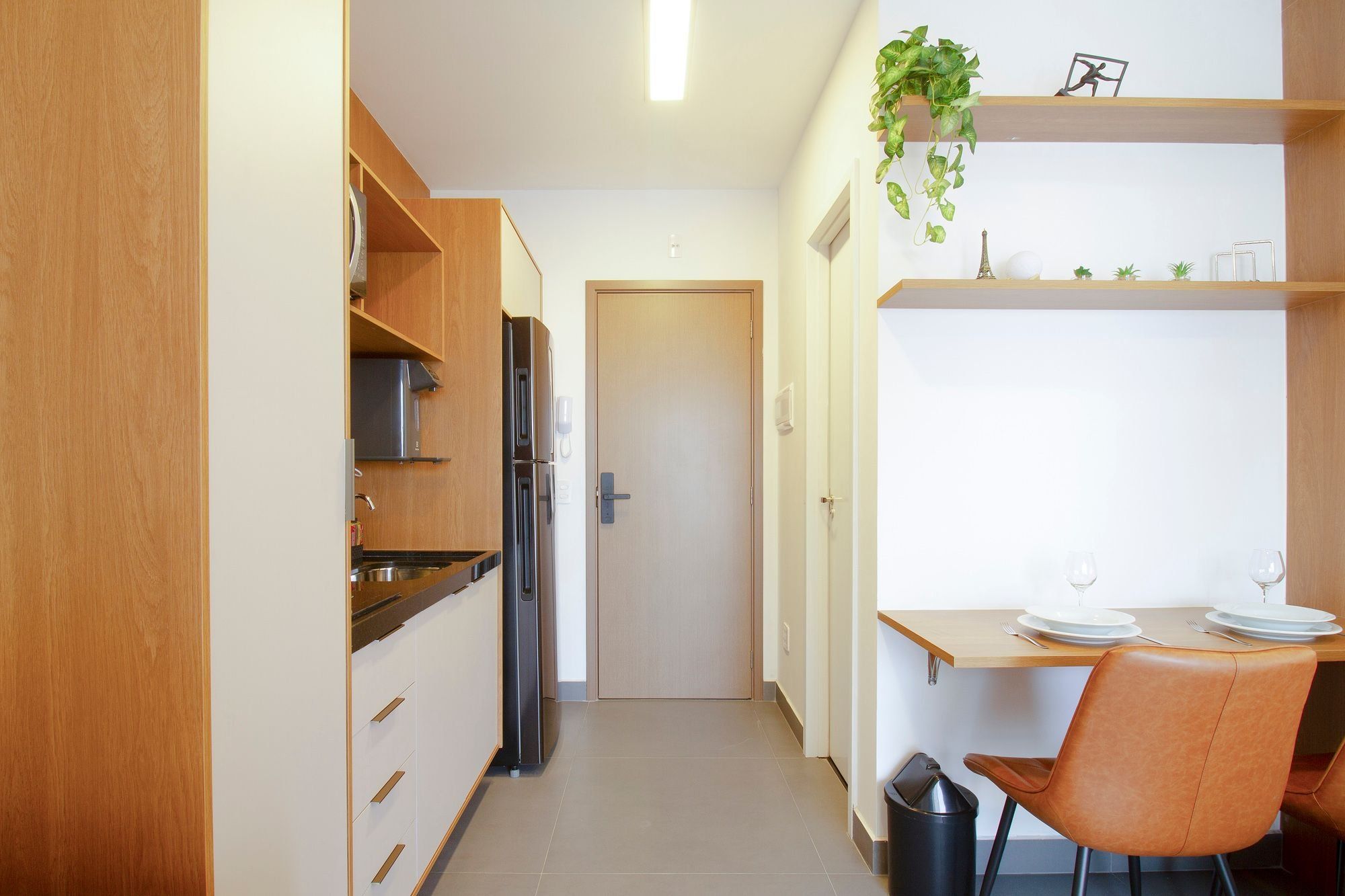 Een functionele keuken met een koelkast, kastjes en een eethoek met een tafel en stoelen.