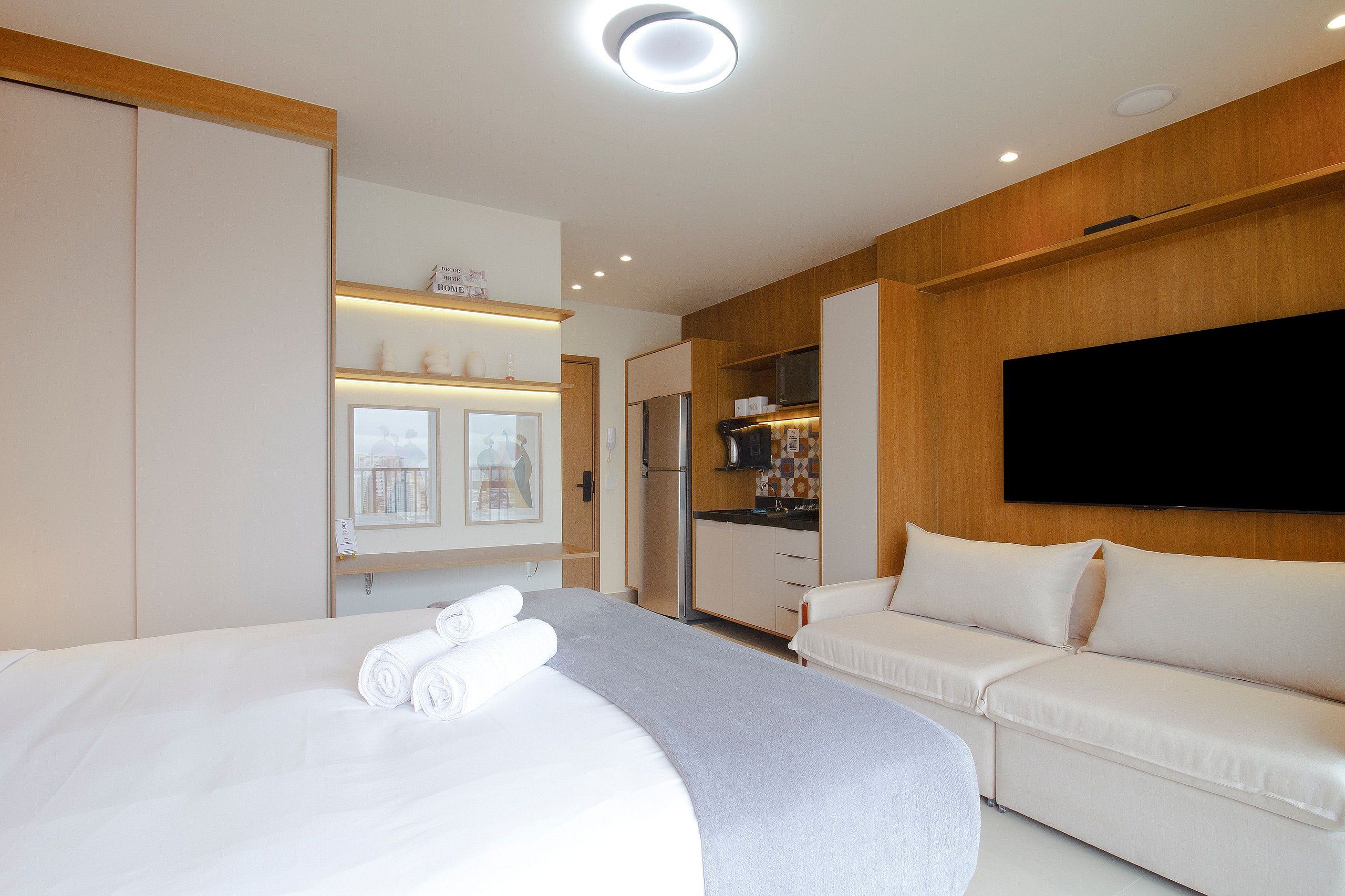 A hotel room with a bed, a sofa, a TV, and a kitchenette.