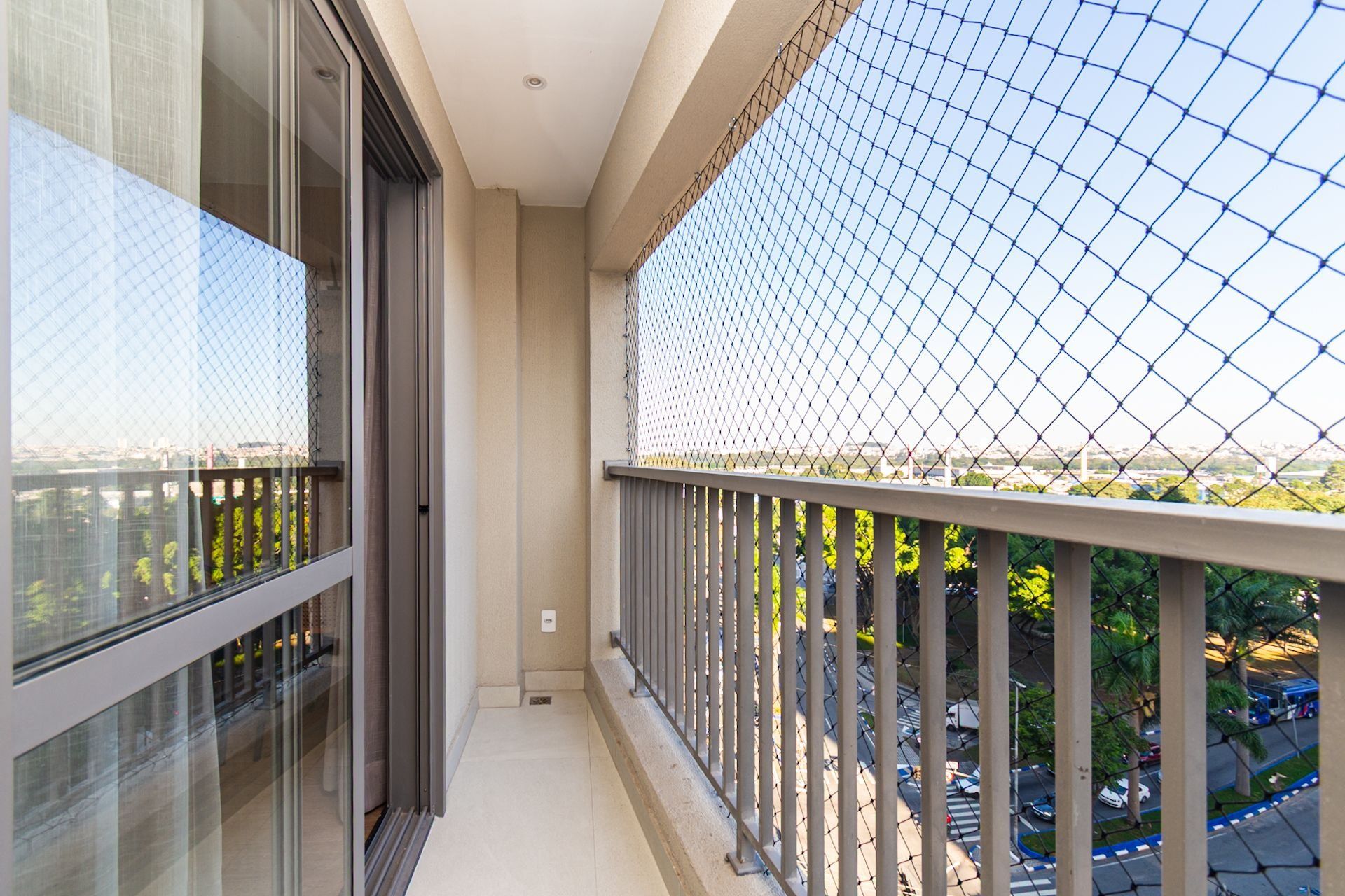 A balcony with a chain-link fence, a glass door, and a view of a cityscape.