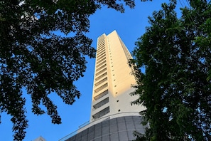 Un edificio alto y moderno con un diseño angular único, rodeado de frondosos árboles verdes.