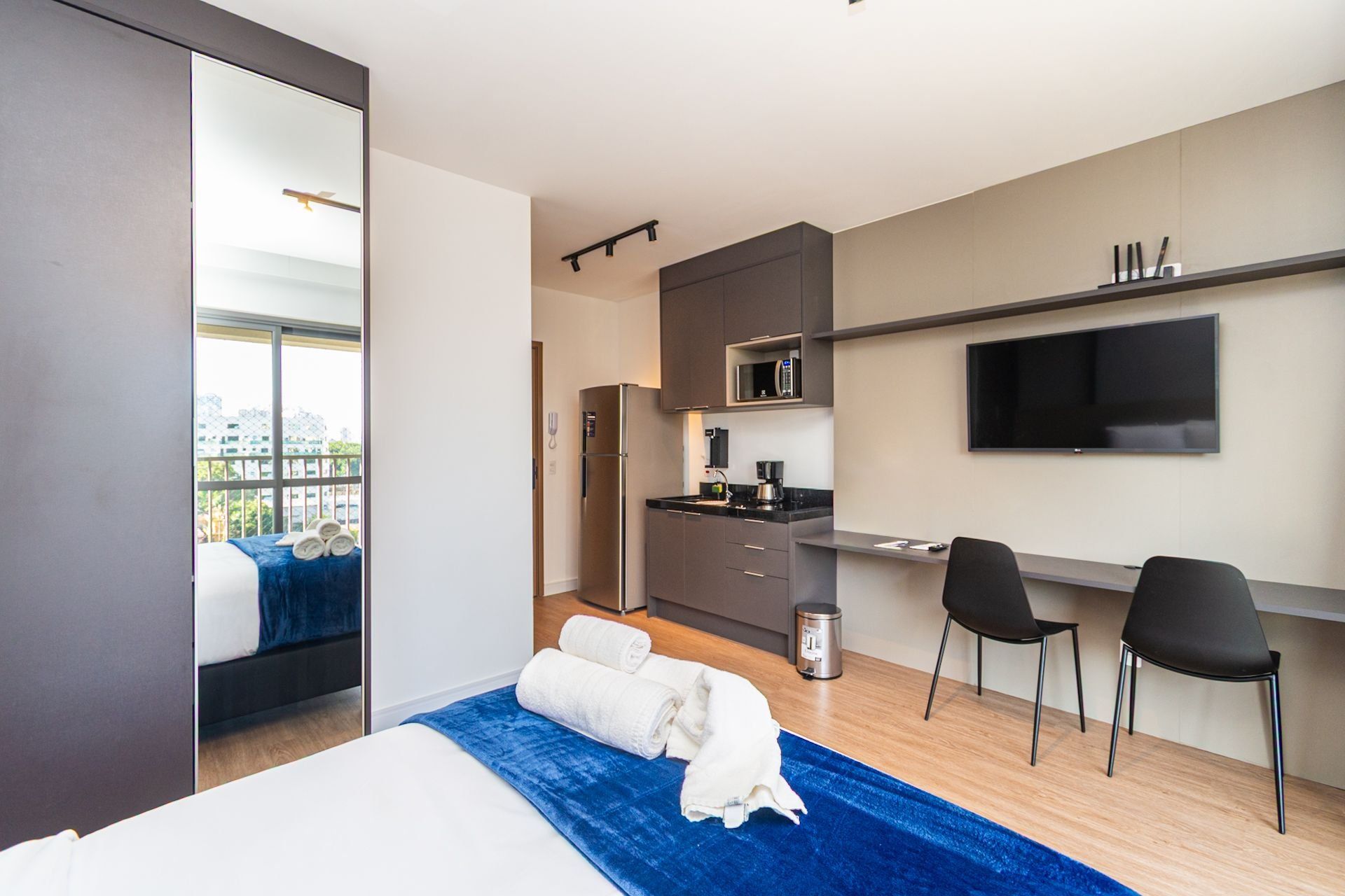 A modern hotel room with a bed, a desk, a microwave, a TV, and a balcony with a view.