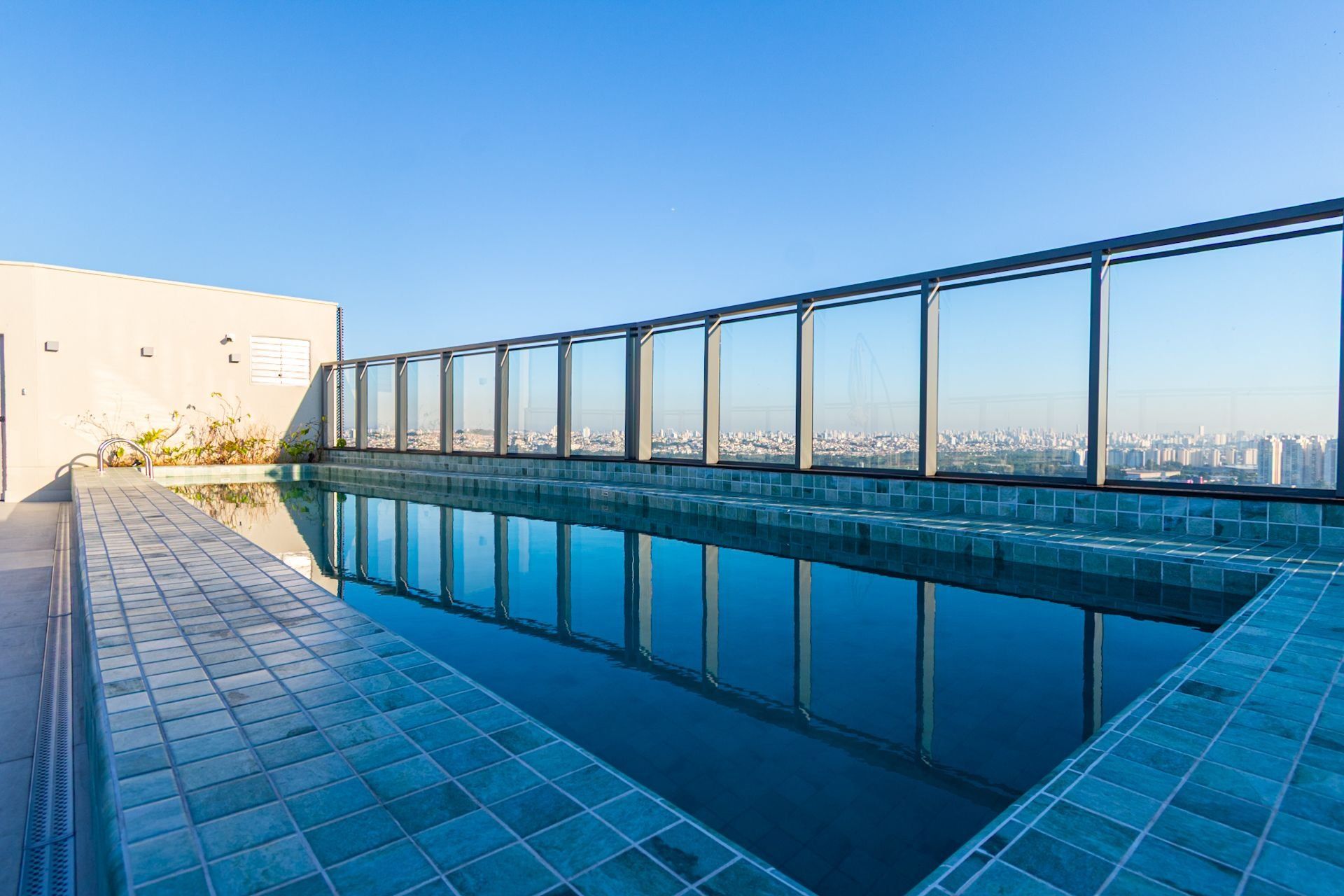 A rooftop swimming pool with a city view, surrounded by a glass railing.
