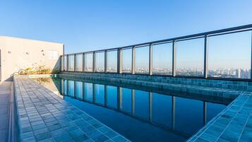 A rooftop swimming pool with a city view, surrounded by a glass railing.