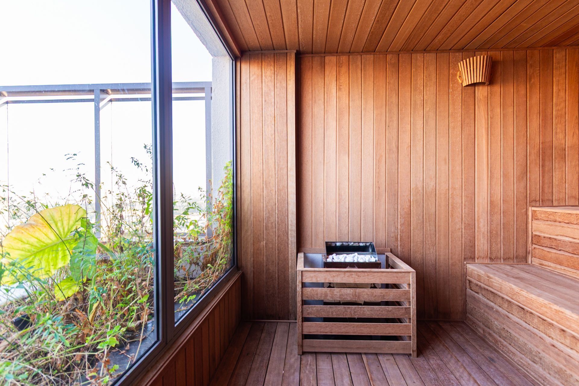 Una sauna con paredes de madera y una ventana, un banco de madera y un caja de madera con objetos.