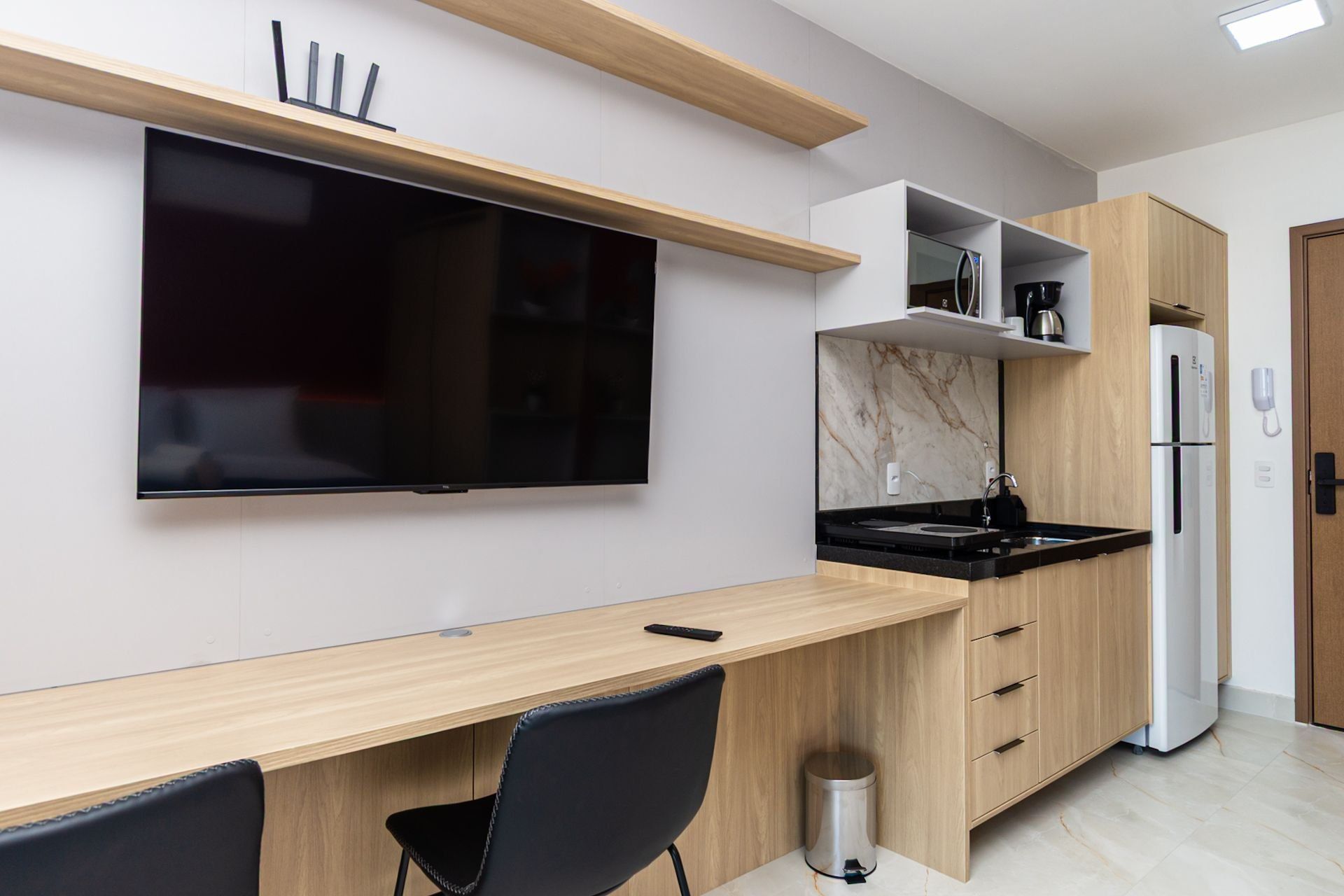 A modern kitchen with a built-in TV, wooden cabinets, a black countertop, and a stainless steel sink.