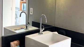 A modern bathroom with a white sink, two faucets, and a large mirror.