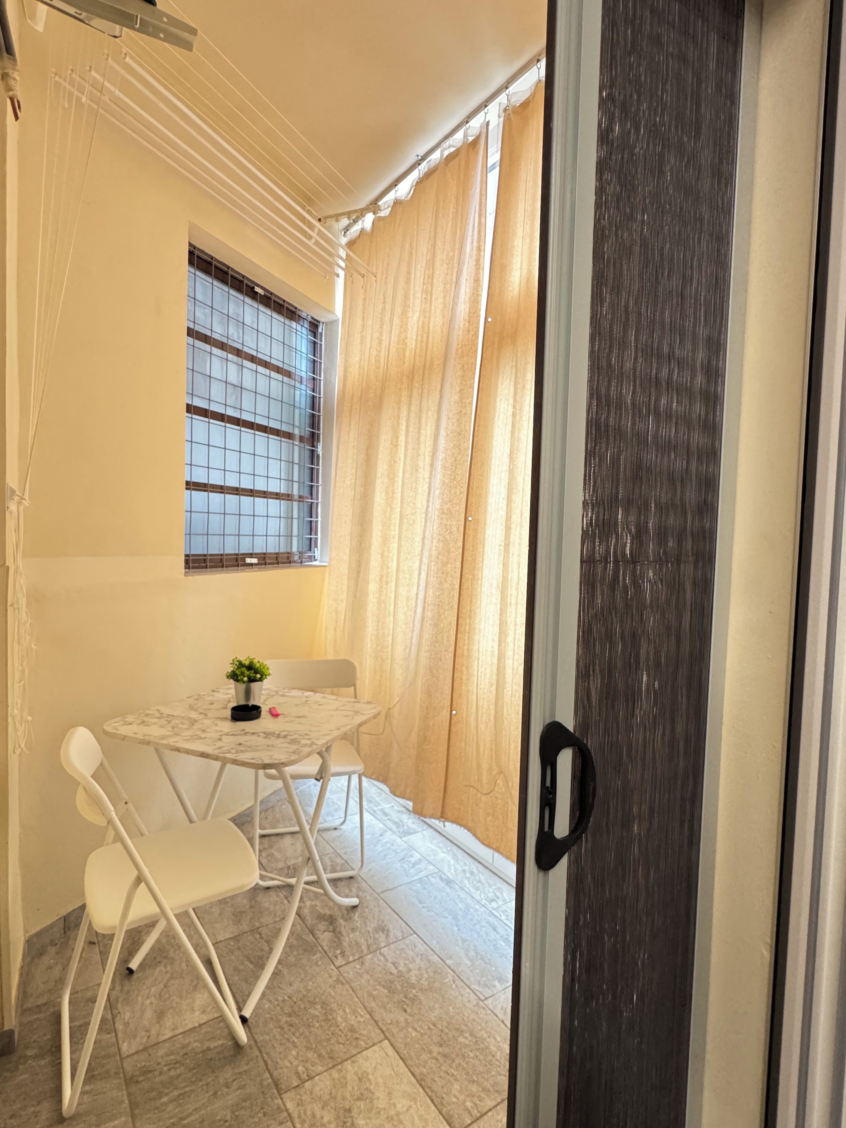 Une petite pièce avec une table et des chaises, une fenêtre grillagée et un rideau.