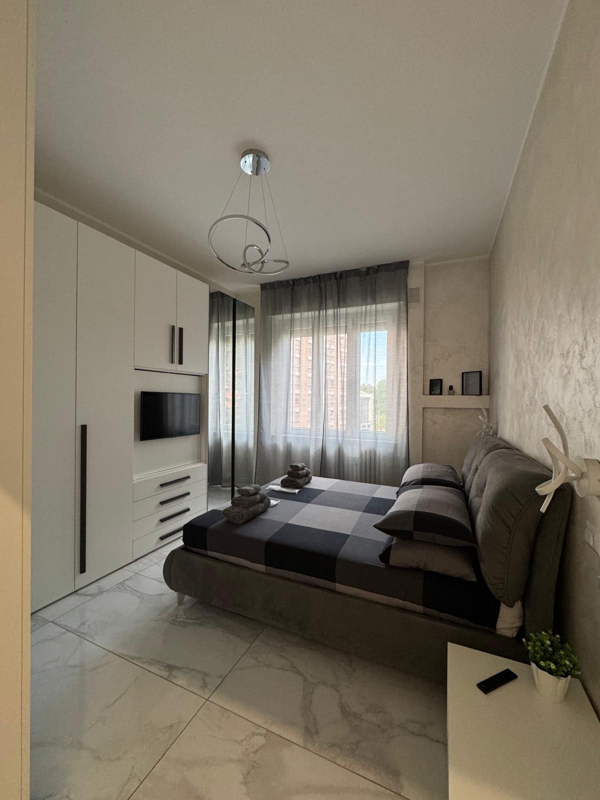 A modern bedroom with a bed, a TV, and a window with curtains.