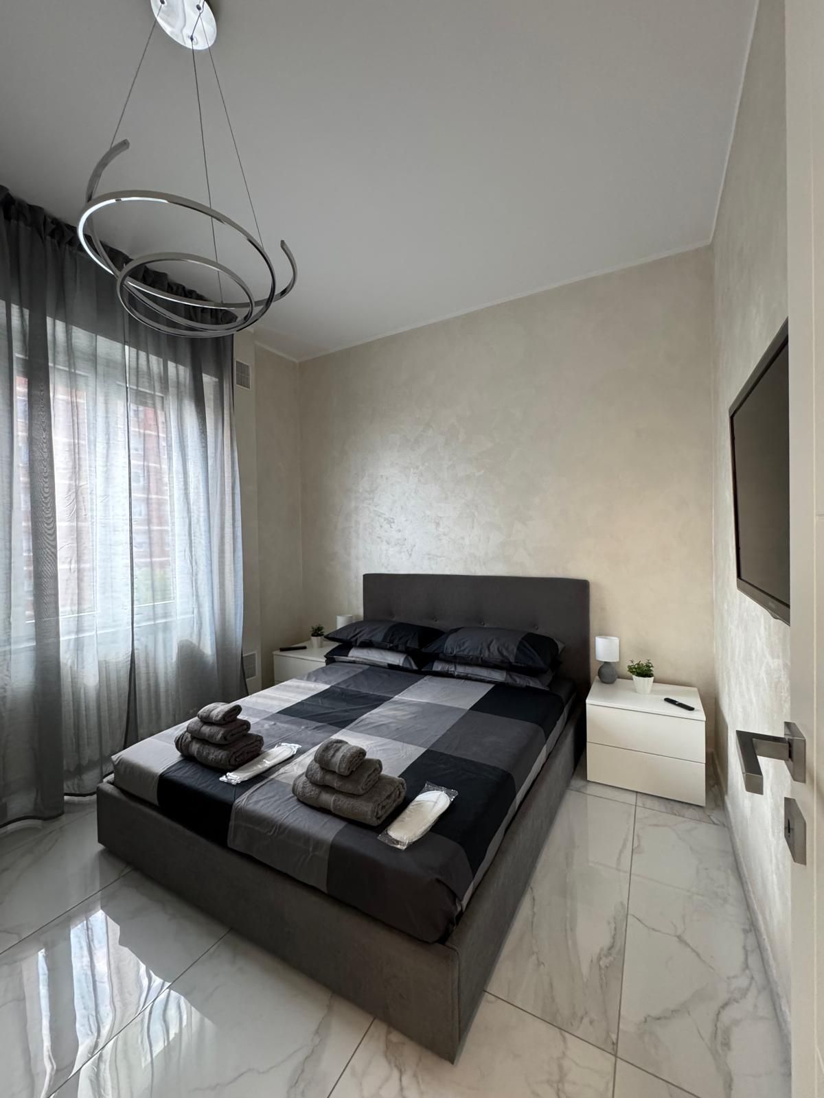 Une chambre à coucher moderne avec un grand lit, une table de chevet, un téléviseur fixé au mur et un luminaire suspendu au plafond.