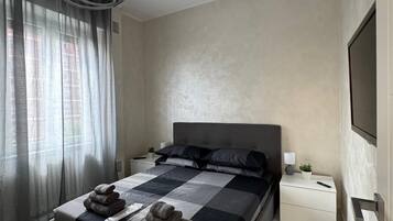 Une chambre à coucher moderne avec un grand lit, une table de chevet, un téléviseur fixé au mur et un luminaire suspendu au plafond.