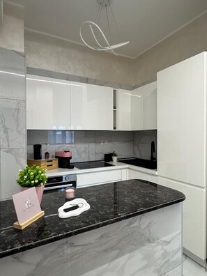 Cozinha moderna com armários brancos, bancada preta e luminária pendente.