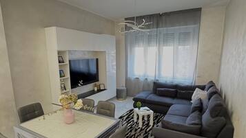 Ein modernes Wohnzimmer mit Essbereich, einer Sofagarnitur, einem Fernseher und einer Deckenleuchte.