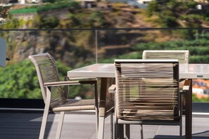 A dining area with a table and chairs on a balcony with a view of a hillside. - GuestReady-Luxurious Retreat in Câmara de Lobos (Câmara de Lobos)