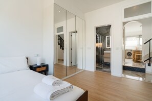 A modern hotel room with a large bed, a bedside table, a mirror, and a view into the bathroom and kitchen area. - GuestReady-Luxurious Retreat in Câmara de Lobos (Câmara de Lobos)