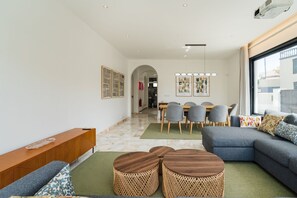A modern living room with a sofa, coffee table, and dining area with chairs. - GuestReady-Luxurious Retreat in Câmara de Lobos (Câmara de Lobos)