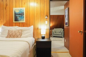 Ein Hotelzimmer mit einem Bett, einem Nachttisch, einer Lampe, einem Sessel und einem Bild an der Wand.