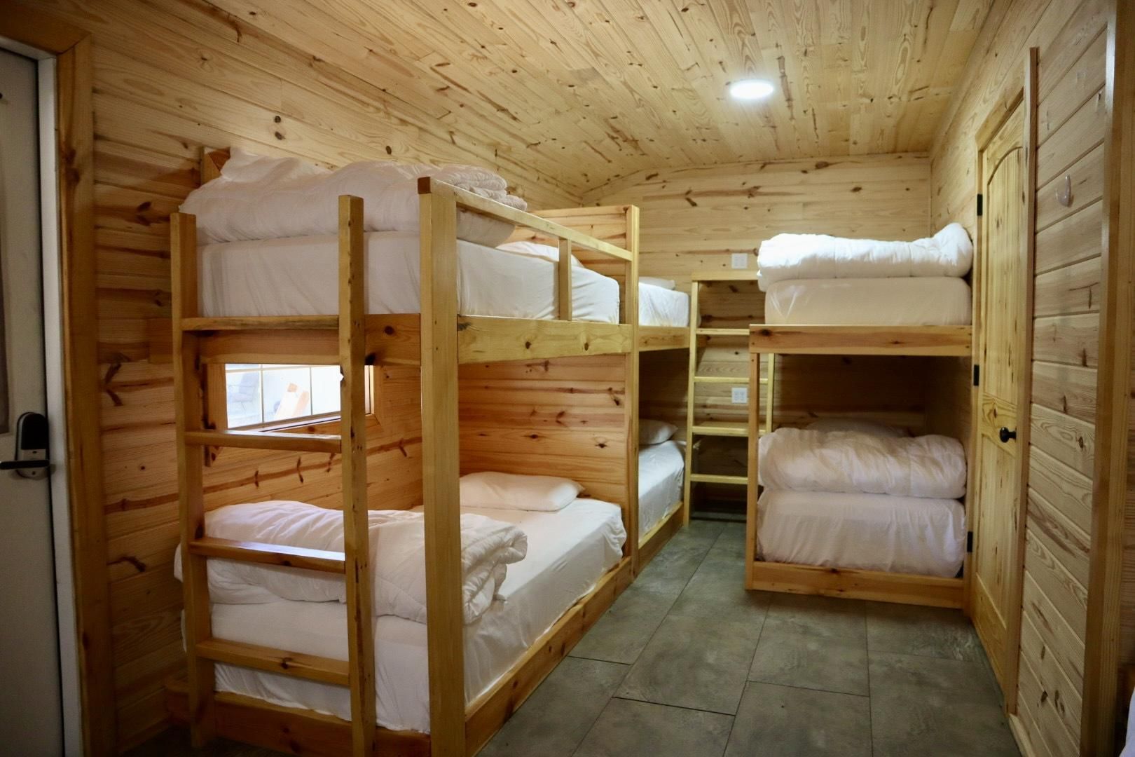 Eine Holzhütte mit Etagenbetten, die in einem zentralen Gang angeordnet sind, einem kleinen Fenster und einer Tür auf der linken Seite.