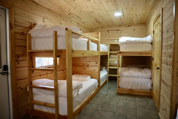 A wooden cabin with bunk beds arranged in a central aisle, a small window, and a door on the left.