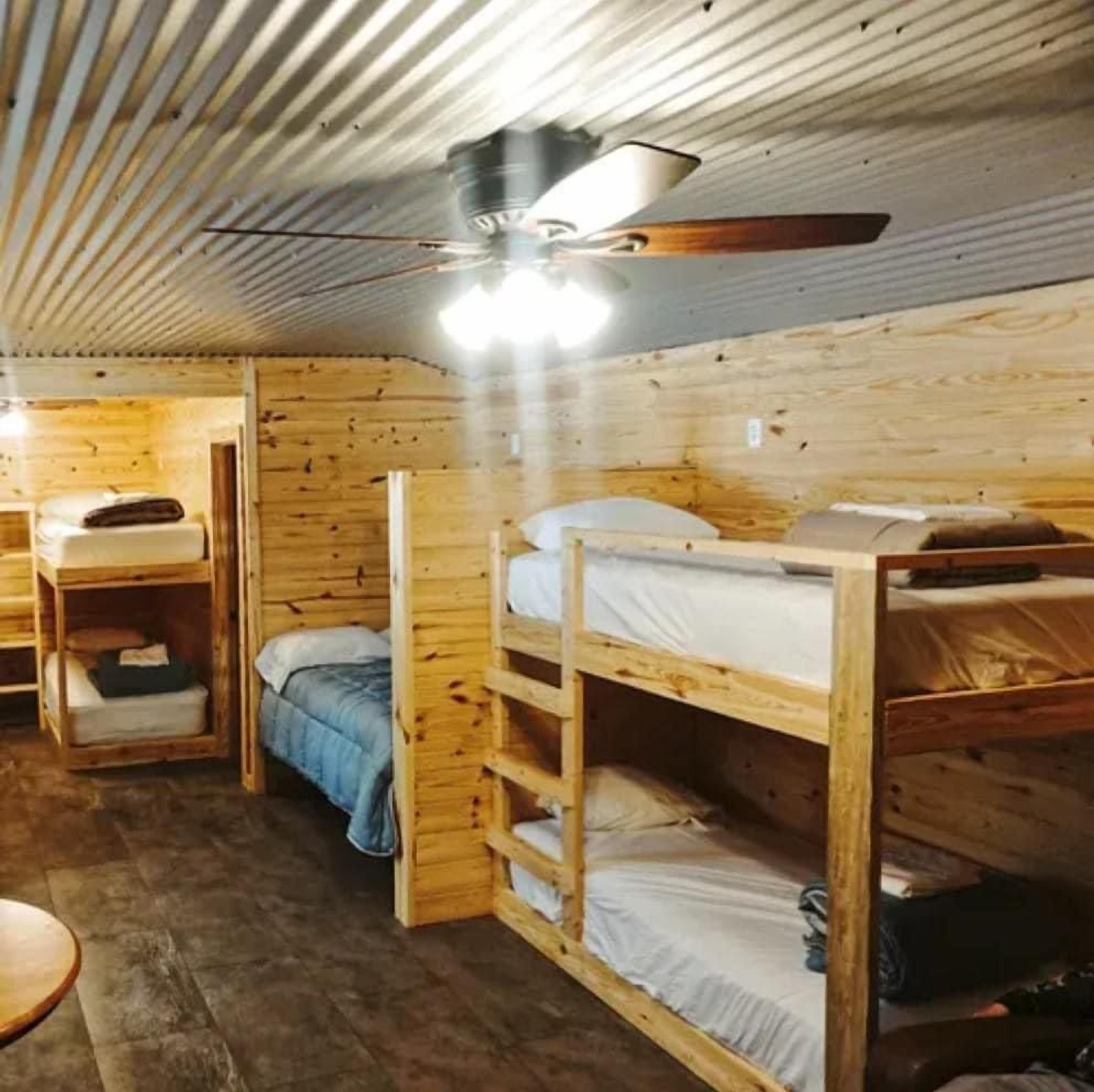 A wooden cabin interior with bunk beds, a ceiling fan, and a round table.