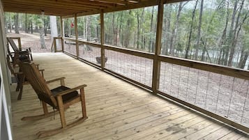 A covered deck with wooden flooring and a view of a forest.