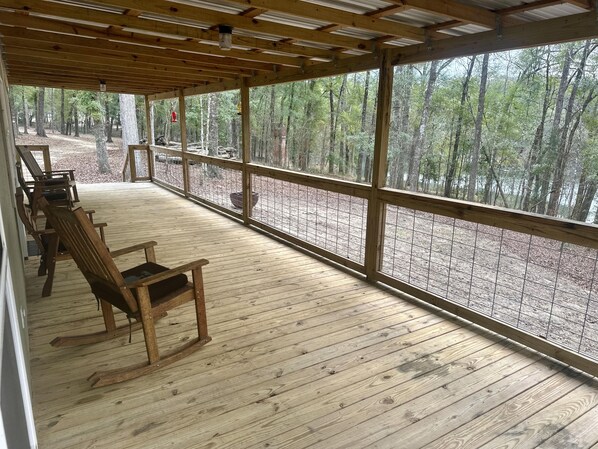 A covered deck with wooden flooring and a view of a forest.