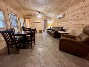 A wooden interior with a dining table, chairs, a sofa, and a small table with a lamp.