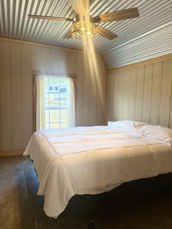A bedroom with a single bed, a ceiling fan, and a window with curtains.