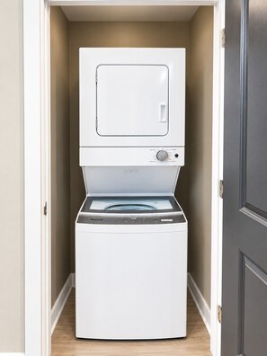 A front-loading washer and dryer unit in a laundry room with a door on the right. - Magic City Outlook | 2 Queen 2BR (Birmingham)