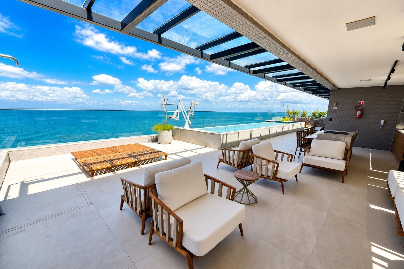 A sunlit outdoor seating area with a view of the ocean, featuring a pool, lounge chairs, and a dining table.