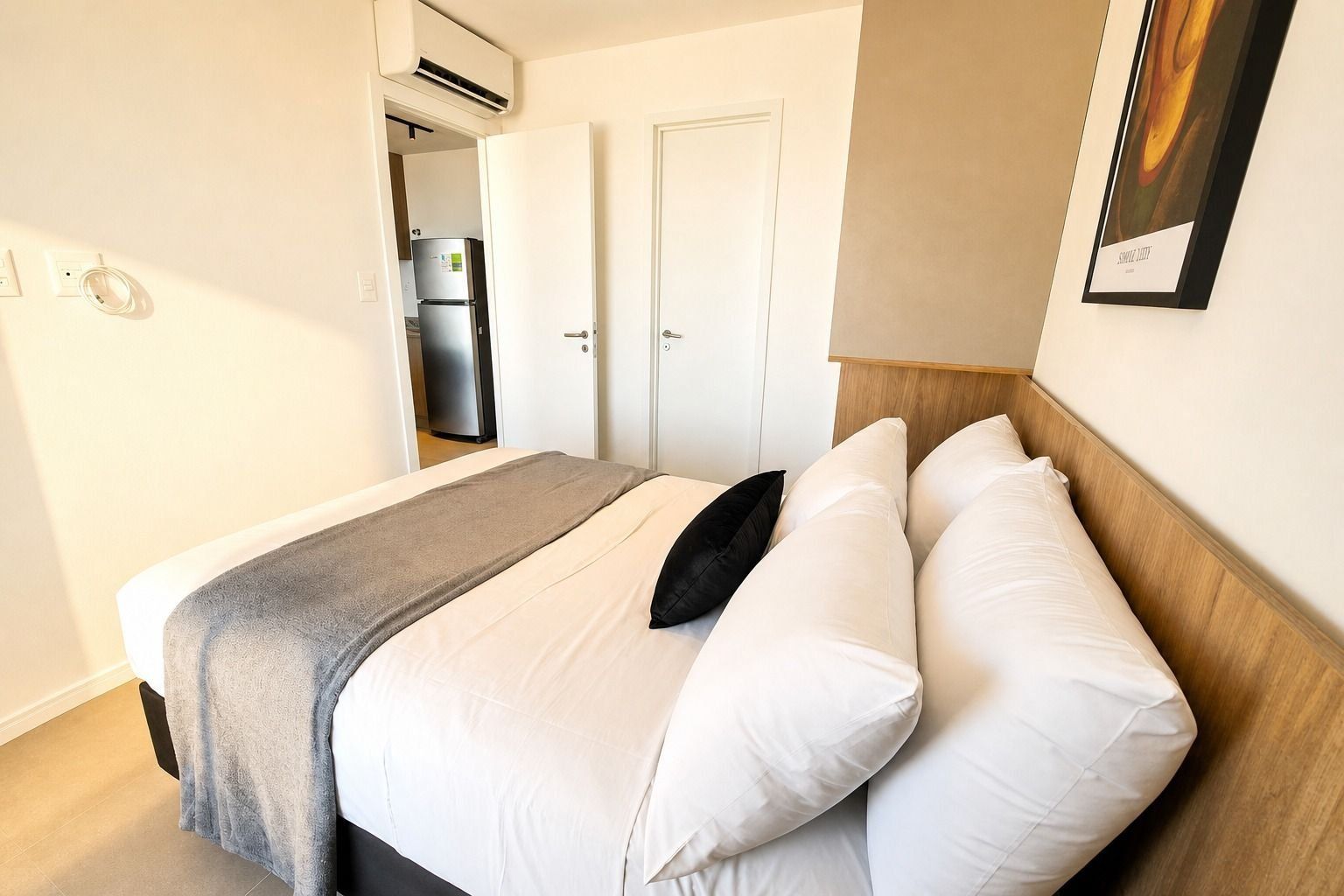 A hotel room with a bed, a door, an air conditioning unit, and a framed picture on the wall.