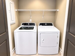 A laundry room with two stacked washers and dryers, a metal shelf above, and a door with a handle. - Magic City Nights | King + Queen 2BR (Birmingham)
