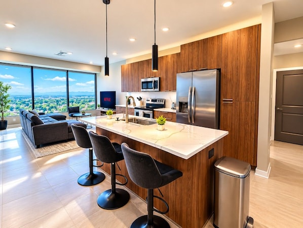 A modern kitchen with a large island, wooden cabinets, stainless steel appliances, and a view of the city. - Magic City Nights | King + Queen 2BR (Birmingham)