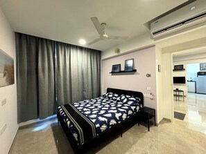 A modern bedroom with a bed, a ceiling fan, and a view into the kitchen. - Finland 1BHK_Hiranandani Estate_City View (Thane)