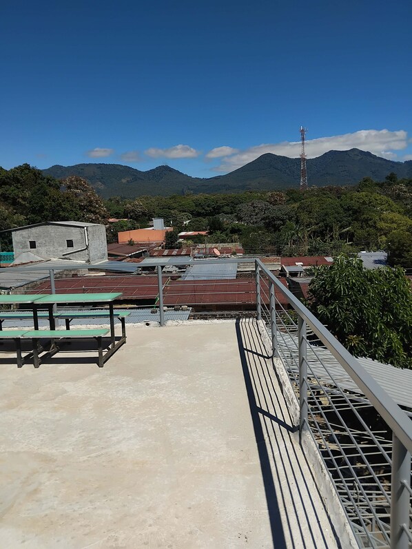 Una terrassa al terrat amb barana de metall, sòl de formigó i vista a un paisatge de muntanyes.