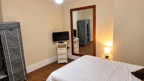 A hotel room with a bed, a television on a stand, a mirror, and a lamp.
