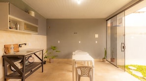 Un baño moderno con ducha, lavamanos y espejo. Hay plantas y un banco en el espacio.