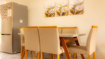 Uma área de refeições com mesa, cadeiras, geladeira e obras de arte nas paredes.
