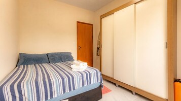 Quarto com cama, almofadas, guarda-roupa e uma porta.