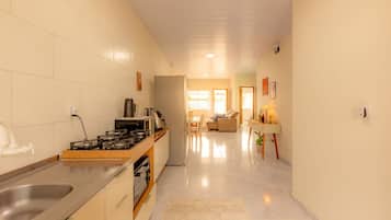 Cozinha moderna com fogão a gás, pia e geladeira. Há uma área de jantar com mesa e cadeiras, e um corredor que leva a uma sala de estar.