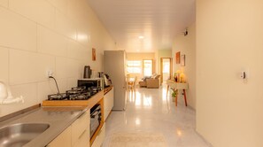 Una cocina moderna con estufa a gas, pileta y refrigerador. Hay un comedor con mesa y sillas, y un pasillo que conduce a una sala de estar.