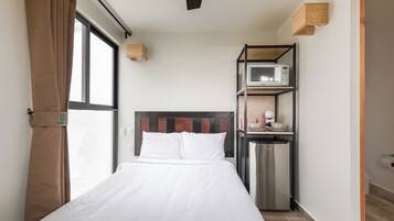 A compact hotel room with a bed, a kitchenette, and a window.