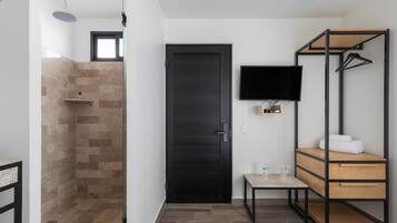 A modern bathroom with a shower, a black door, a mounted TV, and a wooden vanity with towels.