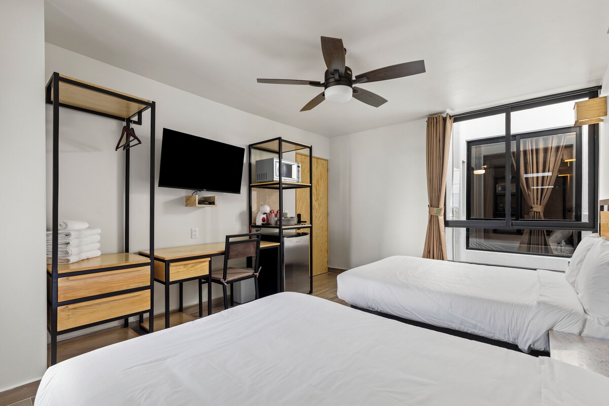 Habitació d'hotel amb llit, escriptori, cadira, televisió, armari i finestra amb cortines.