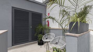 A modern outdoor seating area with two white chairs, a potted plant, and a fire extinguisher on a white wall.