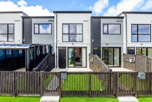 A modern residential building with a flat roof, large windows, and a wooden fence. - Enjoy the convenience of being close to Auckland Airport. (Auckland)