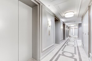 Ein Hotelgang mit Türen auf beiden Seiten, Leuchten an der Decke und einem gemusterten Teppich.