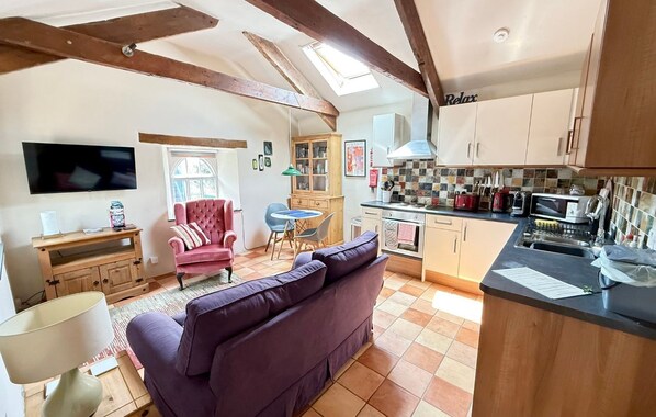 A cozy living room with a sofa, a television, and a dining area with chairs and a table. - Charming Barn Conversion | Dog Friendly | Sleeps 4 (Cornwall)