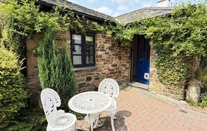 A stone building with a blue door, a window, and a sign that reads 'The Barn.' There are two white outdoor tables and chairs. - Charming Barn Conversion | Dog Friendly | Sleeps 4 (Cornwall)