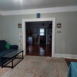 Una sala de estar con un sofá, una mesita de centro y una alfombra. Se ve un acceso a otra habitación.